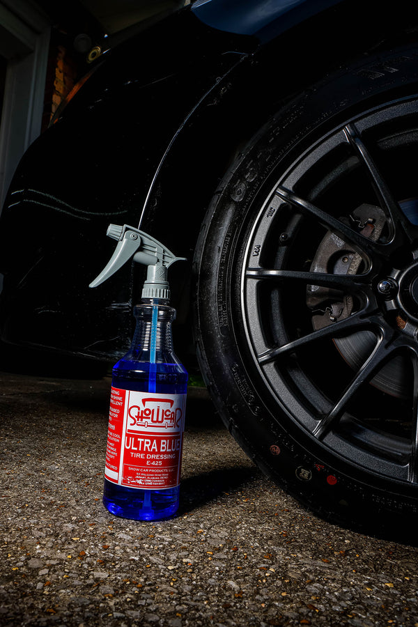 Bottle of Shellhoos Ultra Black tire dressing next to a car tire on a dark background